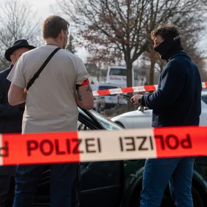 Drei Personen stehen hinter einer Absperrung auf der „Polizei“ steht.