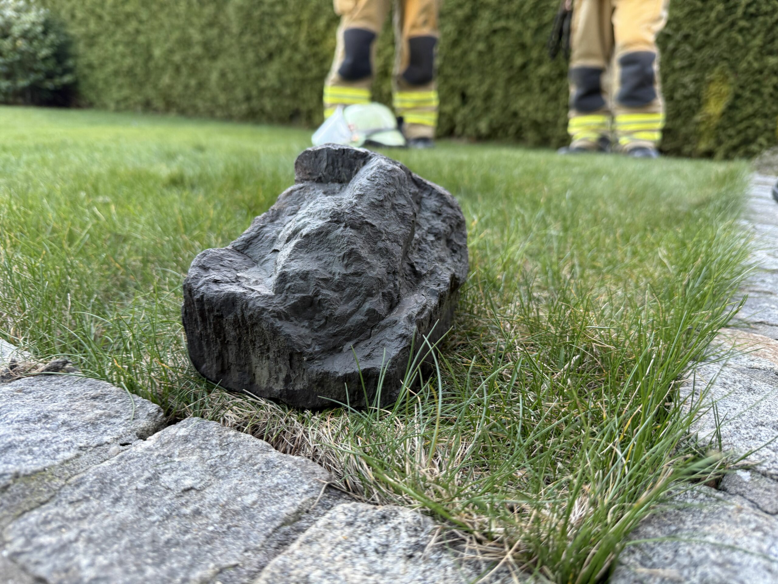 Ein Stein mit ungewöhnlicher Form liegt auf dem Rasen. Im Hintergrund sieht man uniformierte Feuerwehrleute.