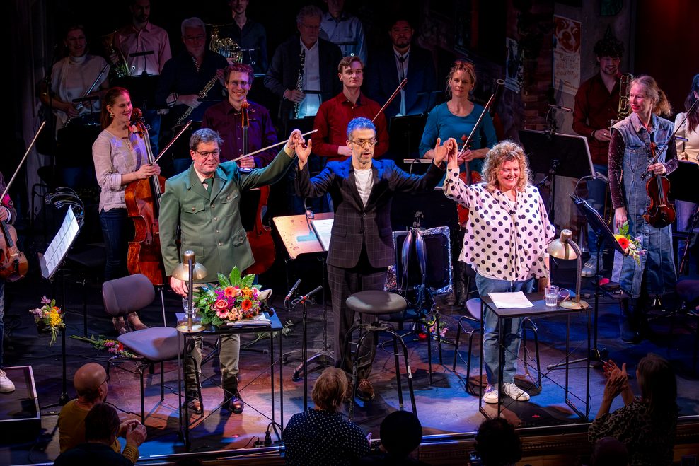 Bühne nach dem Stück, Orchester, vor ihnen die drei Menschen, die sich an den Händen halten