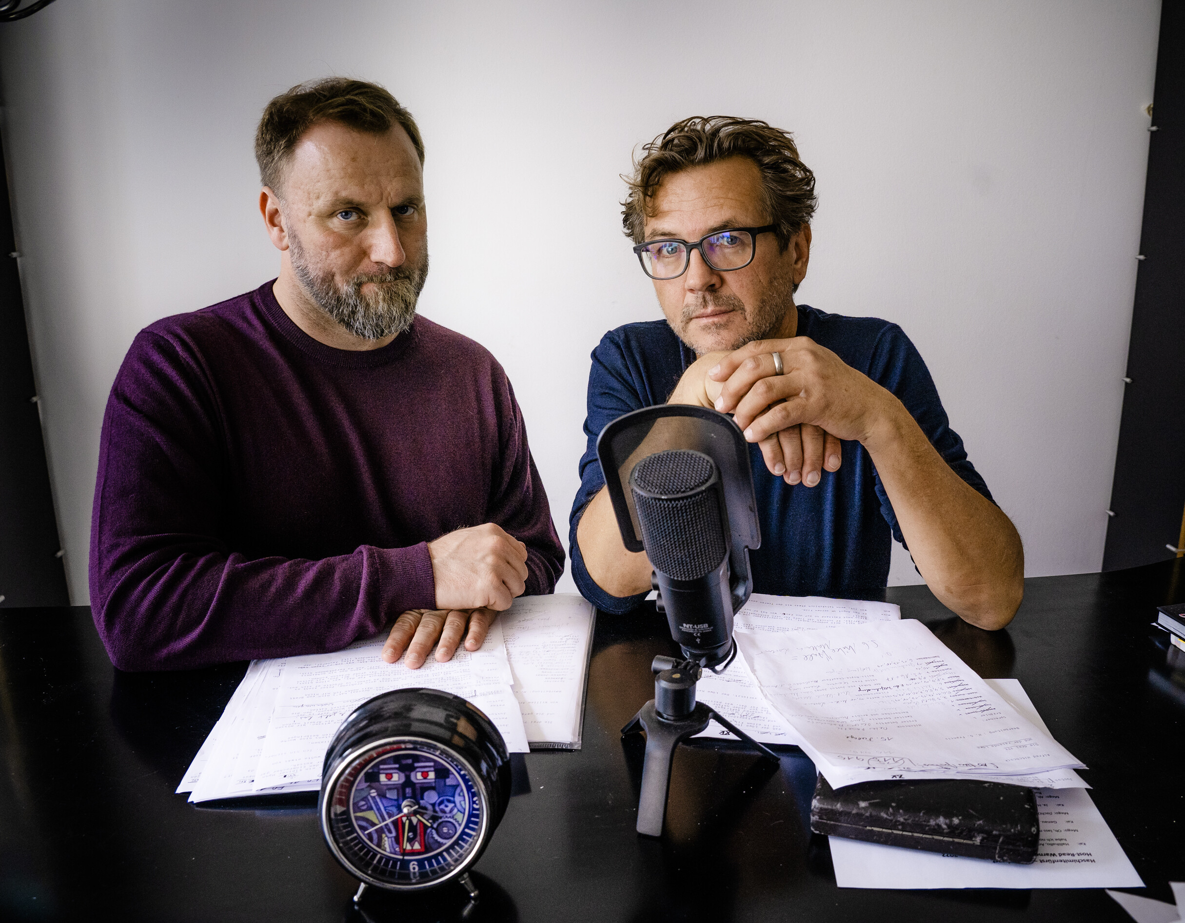 Zwei Männer sitzen an einem Tisch vor einem Podcast-Mikrofon.