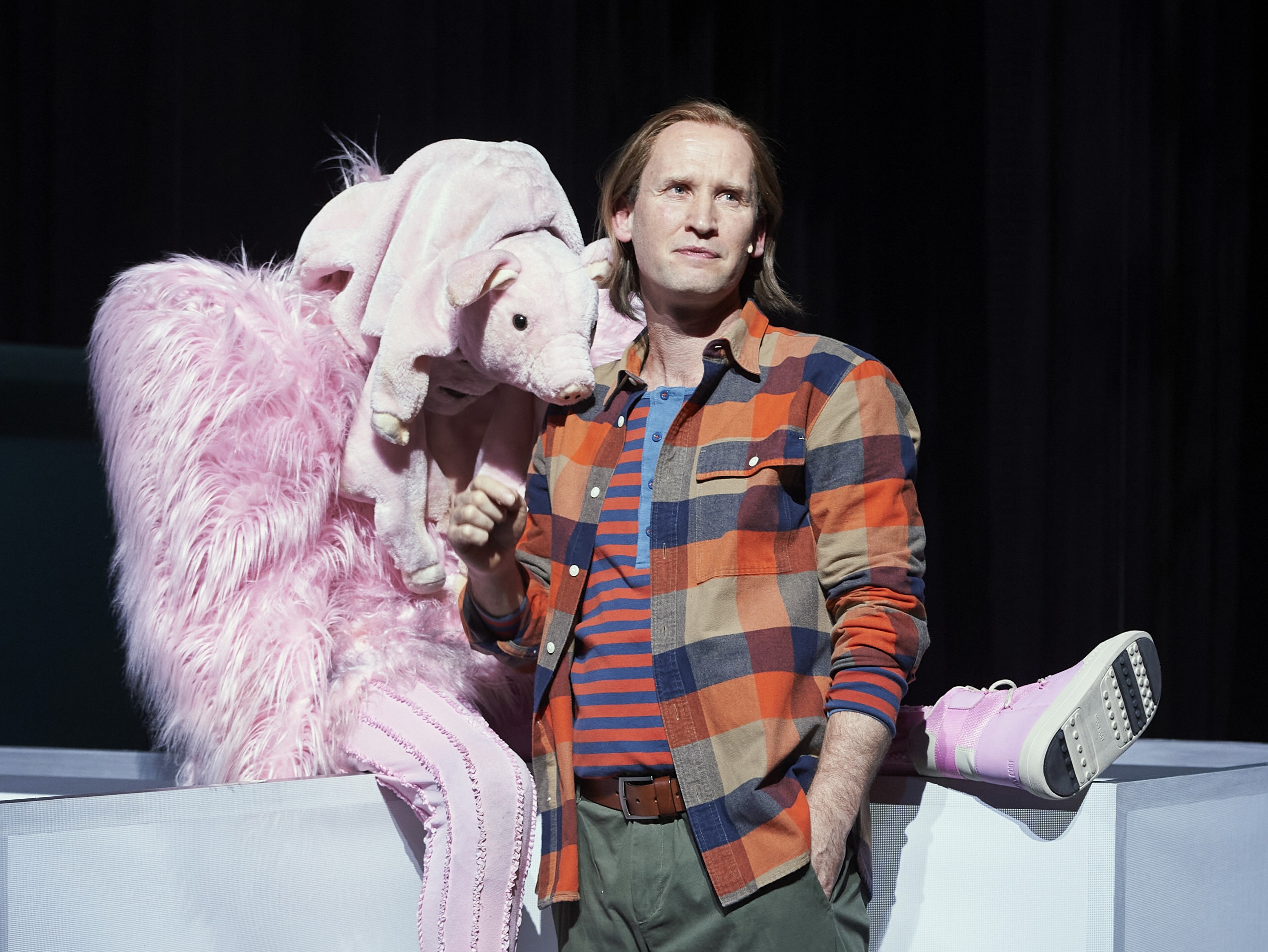 Szene aus dem Theaterstück im Thalia in der Gaußstraße: Ein Mann steht rechts, links neben ihm sitzt ein Mensch im rosafarbenen Plüschkostüm mit einem Stoffschwein als Kopf