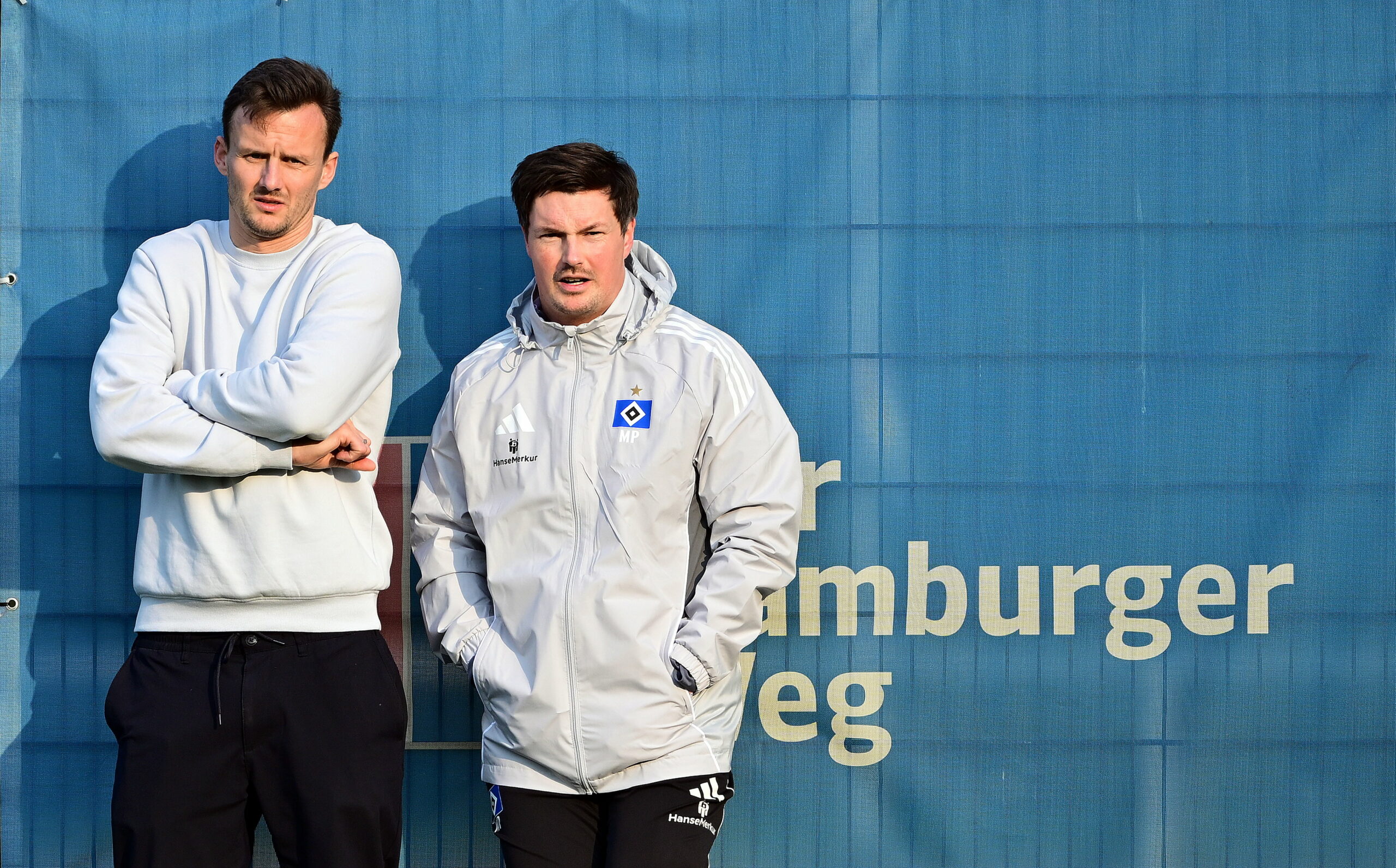 Claus Costa und Merlin Polzin lehnen an einem Zaun am HSV-Trainingsplatz