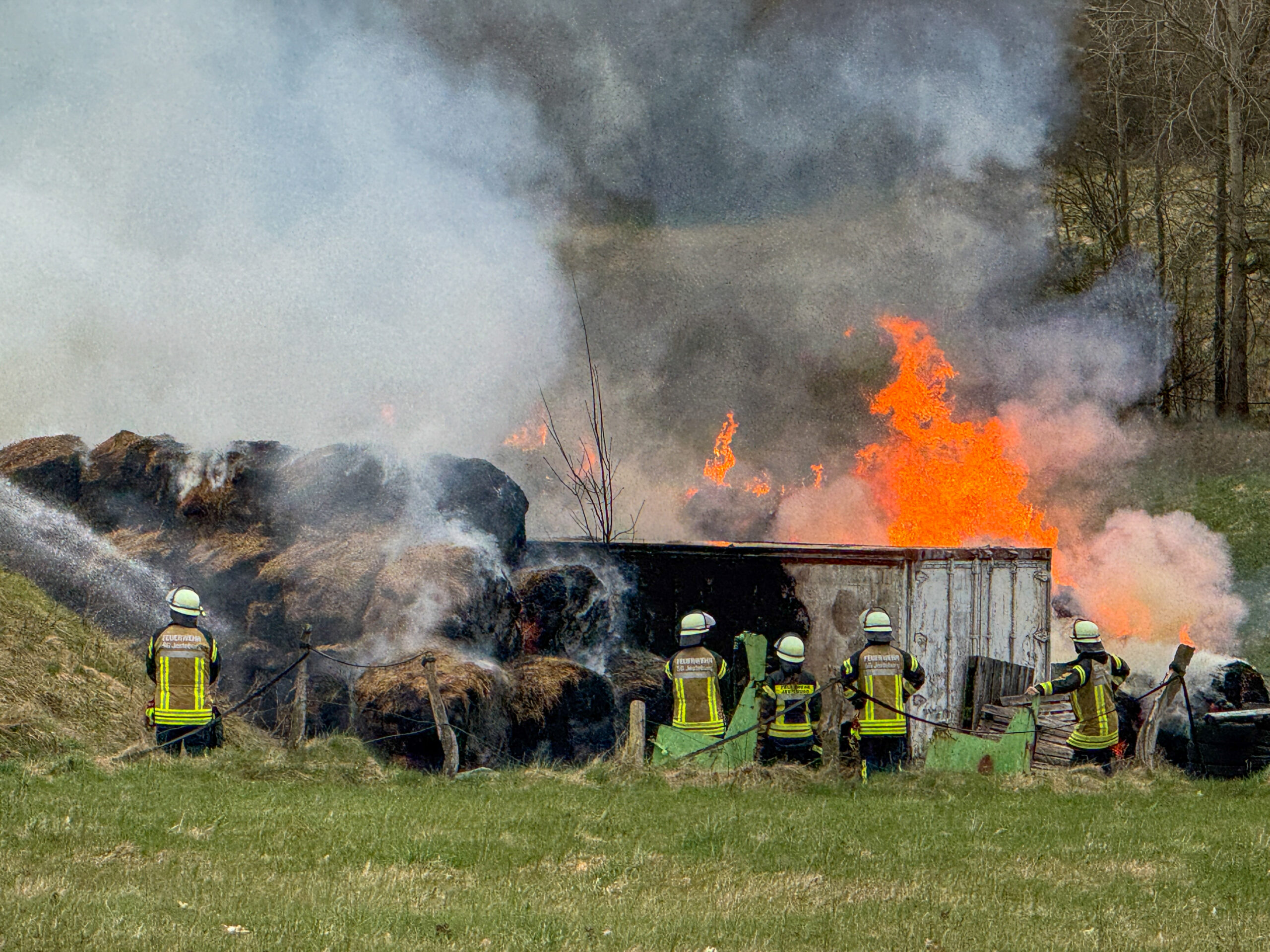 Einsatzkräfte der Feuerwehr stehen auf einem Feld. Über ihnen lodern Flammen.