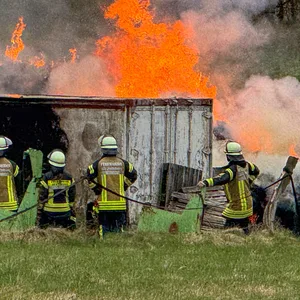 Einsatzkräfte der Feuerwehr stehen auf einem Feld. Über ihnen lodern Flammen.