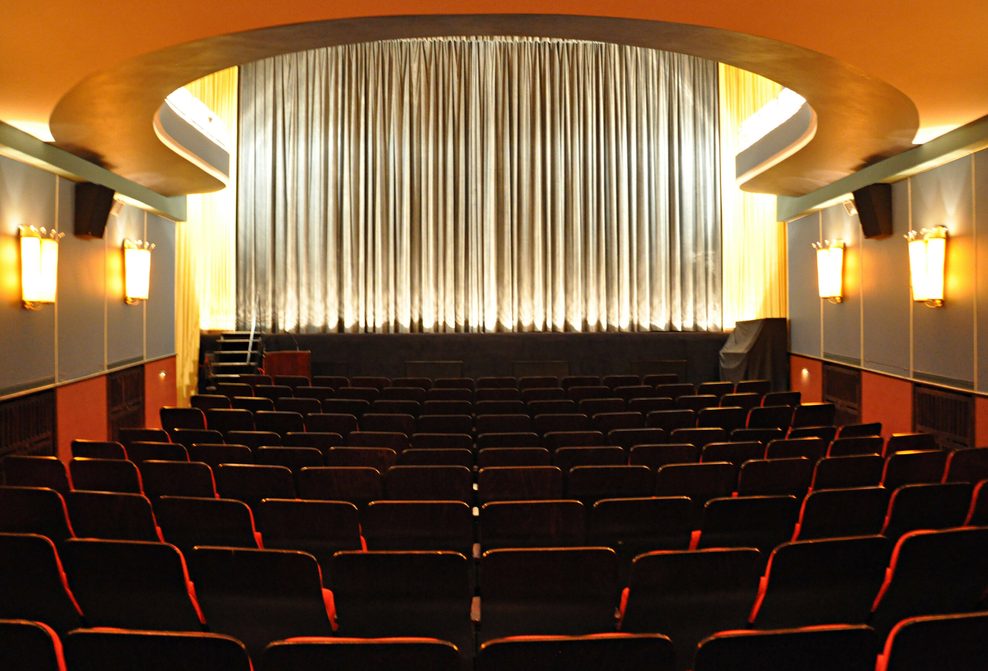 Innenaufnahme eines Kinosaals im Metropolis Kino Hamburg mit roten Sitzen und geschlossener Leinwand vor Beginn einer Vorstellung.