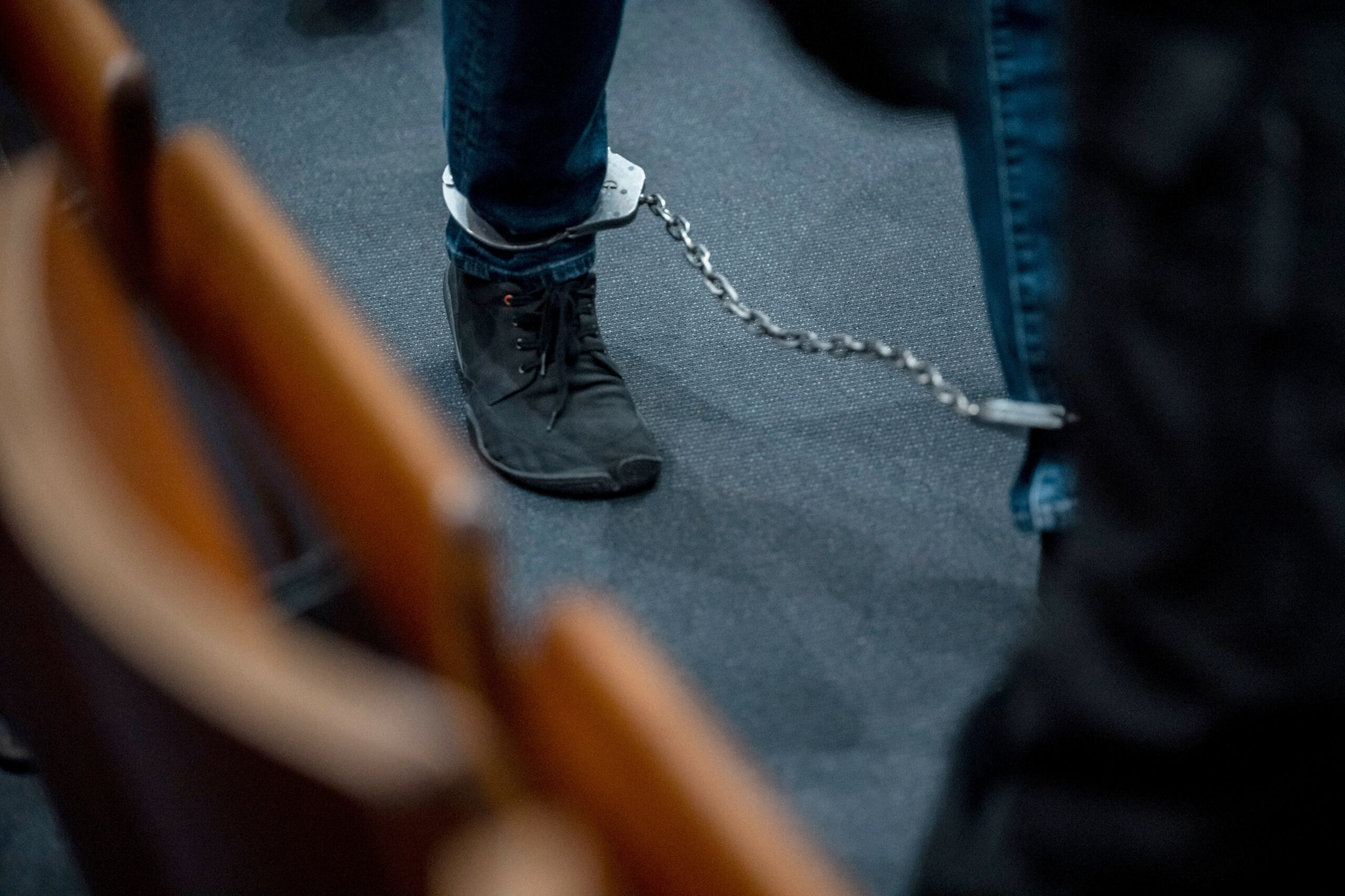Eine Person läuft mit Fußfesseln durch einen Gerichtssaal.