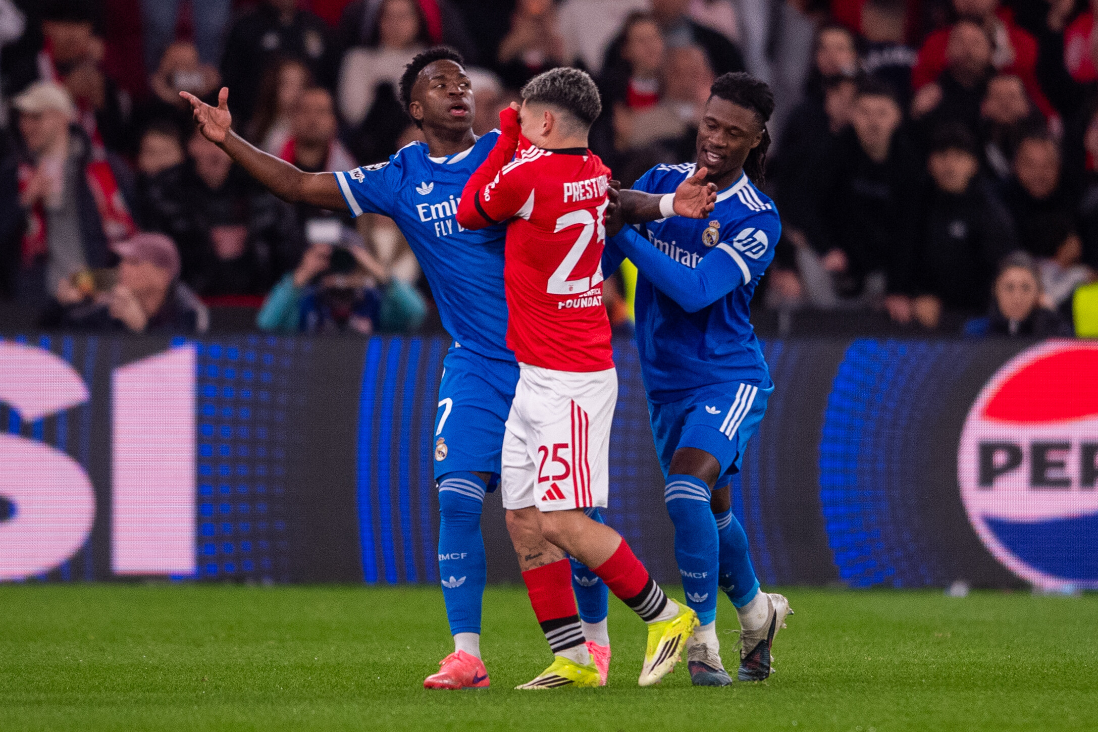 Gianluca Prestianni hält sich das Trikot über den Mund und sagt etwas zu Vinicius Junior