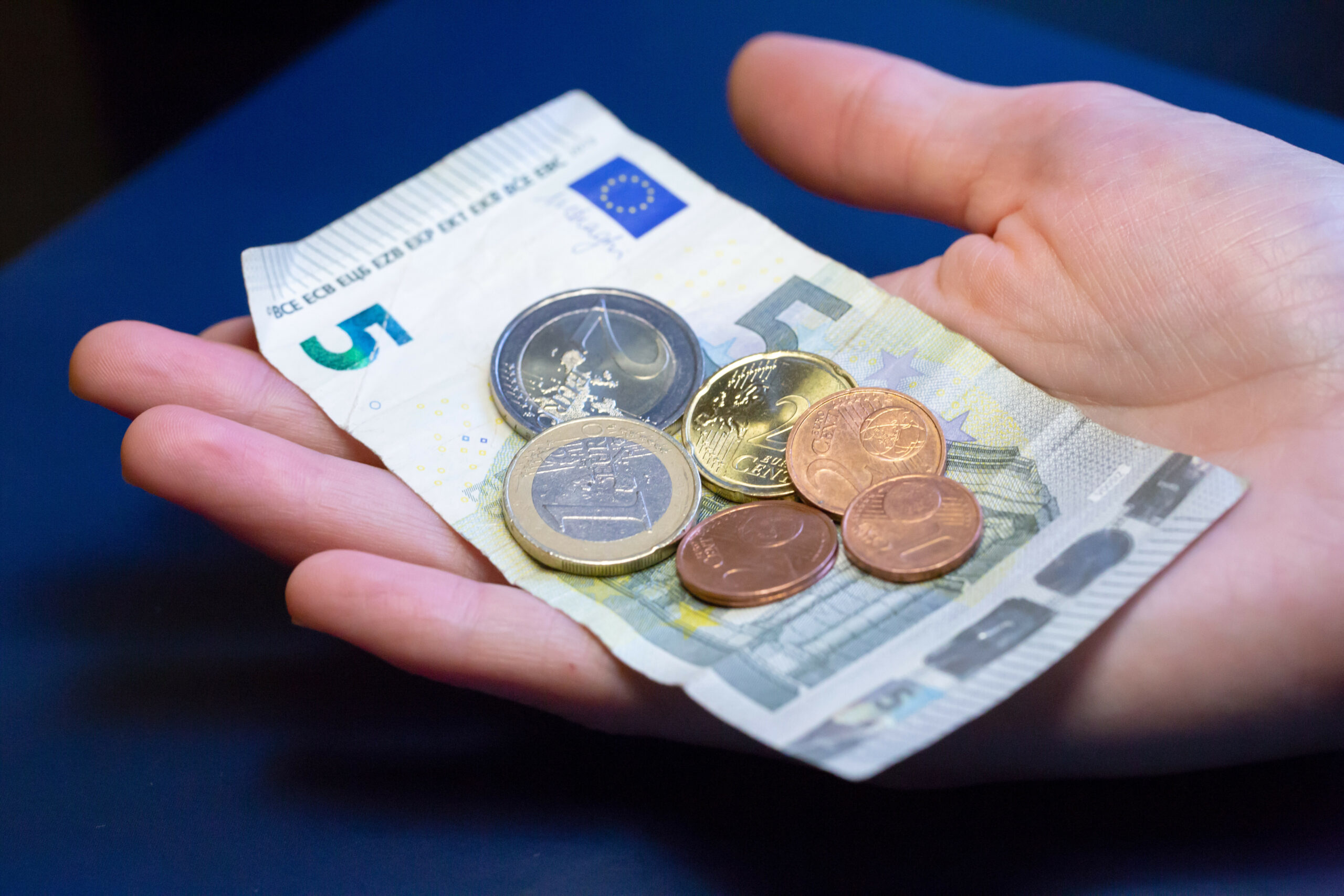 Eine Hand hält einen 5-Euro-Schein und Münzen.