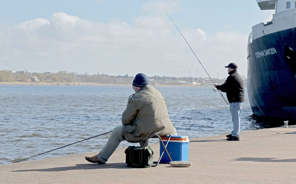 Heringsangler stehen und sitzen an der Kaikante im Stadthafen an der Warnow.