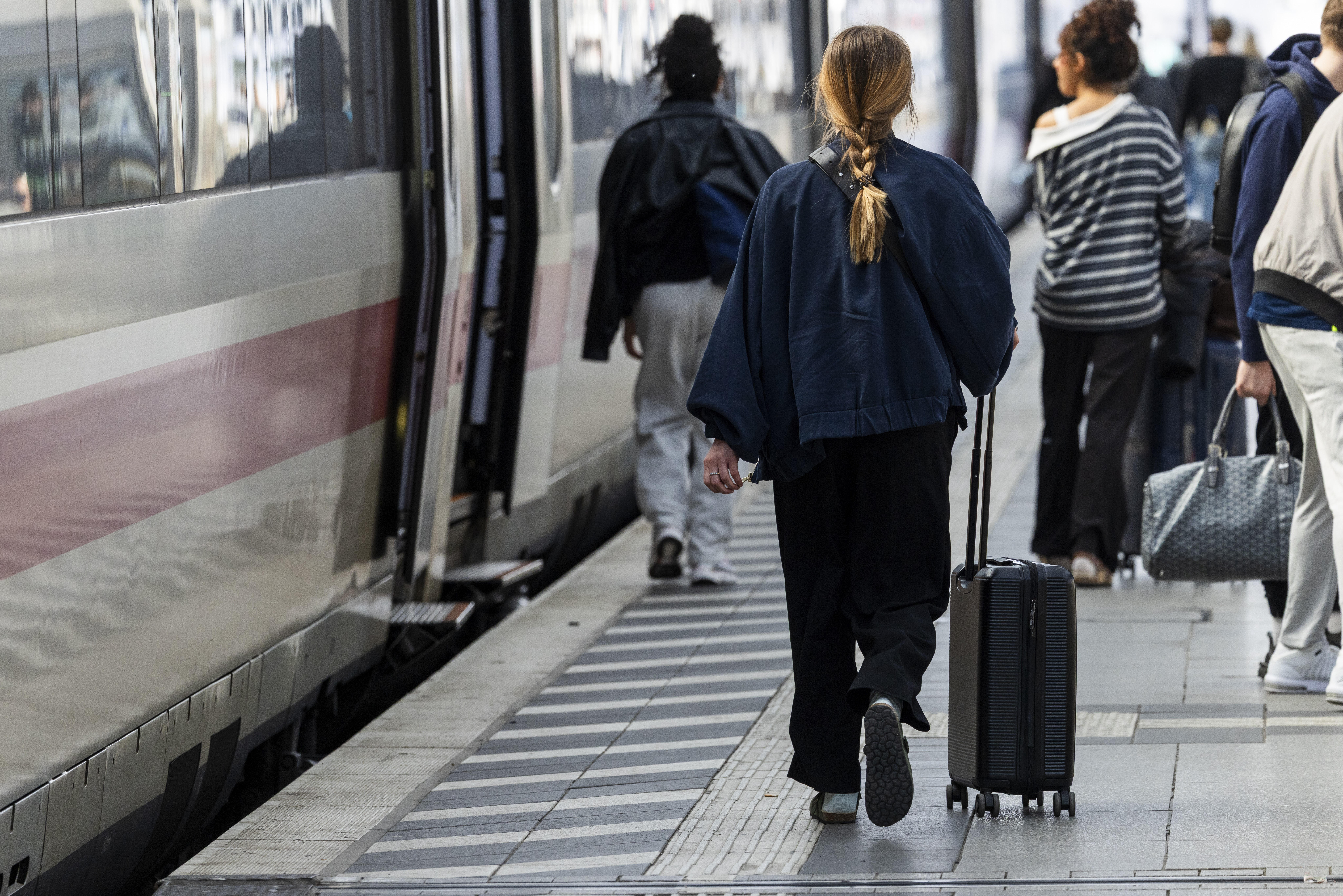 Frau mit ihrem Rollkoffer im Kölner Hauptbahnhof auf einem Gleis mit einem wartenden Zug