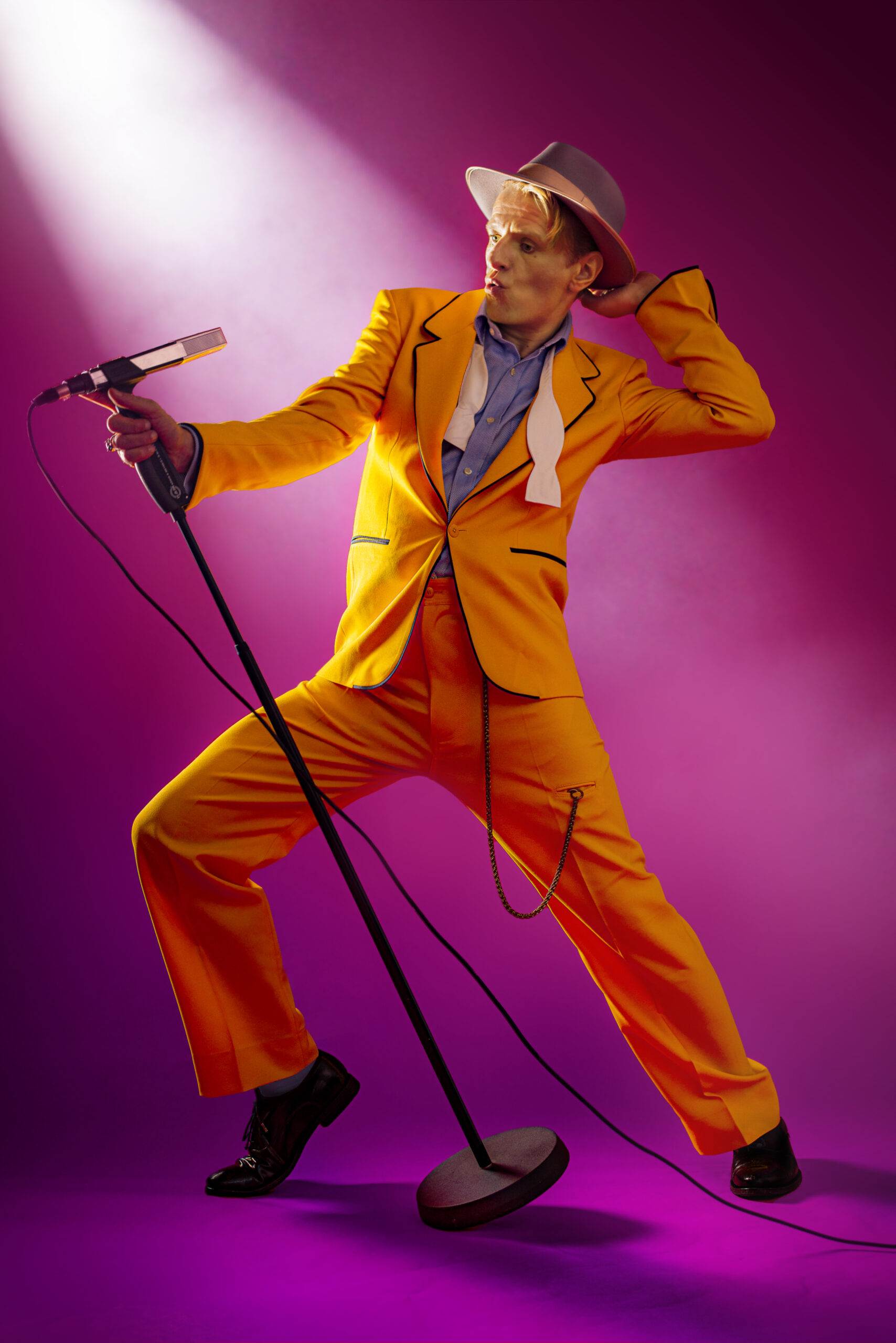 Alexander Scheer steht in einem orangenen Anzug an einem Mikrofon.