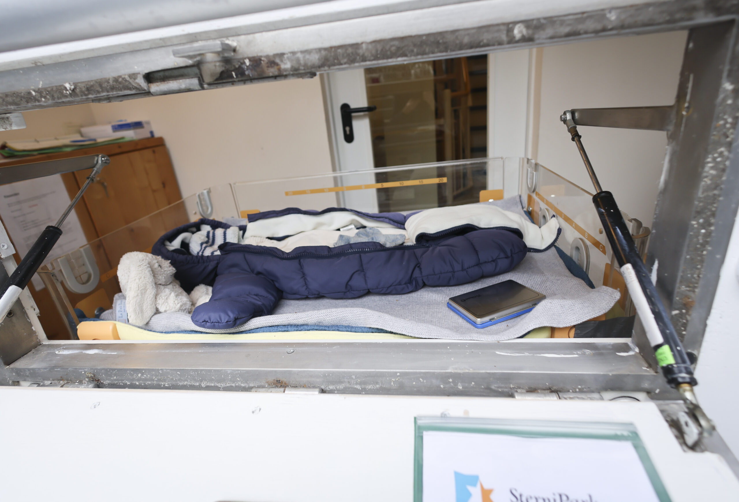 Eine Babyausstattung mit Schlafsack, Strampelanzug, Mütze und Kuscheltieren liegt in einem Wärmebett der Babyklappe im Kinderhaus Goethestraße in Hamburg-Altona.