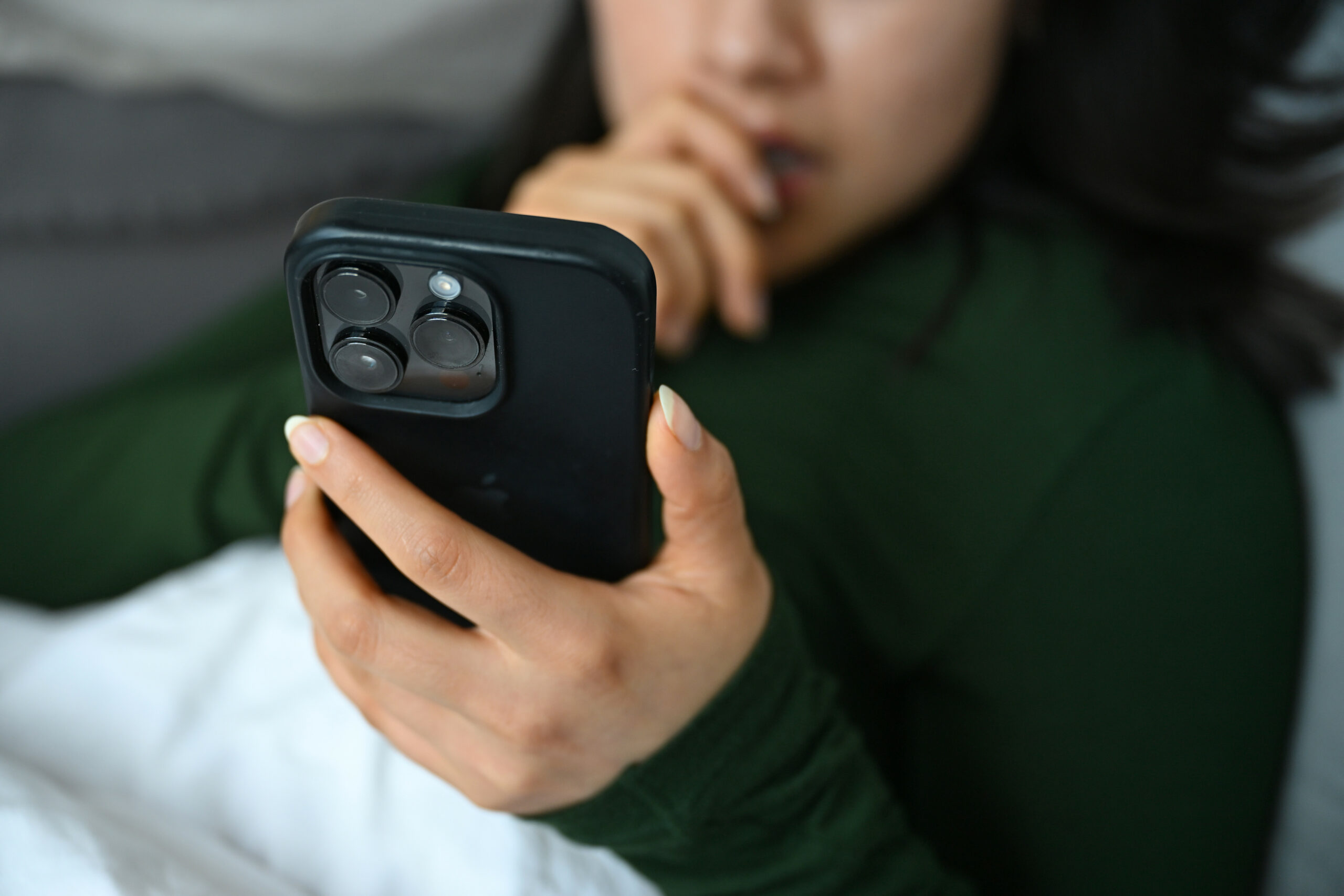 Eine junge Frau liegt mit ihrem Handy auf der Couch und blickt auf das Display.