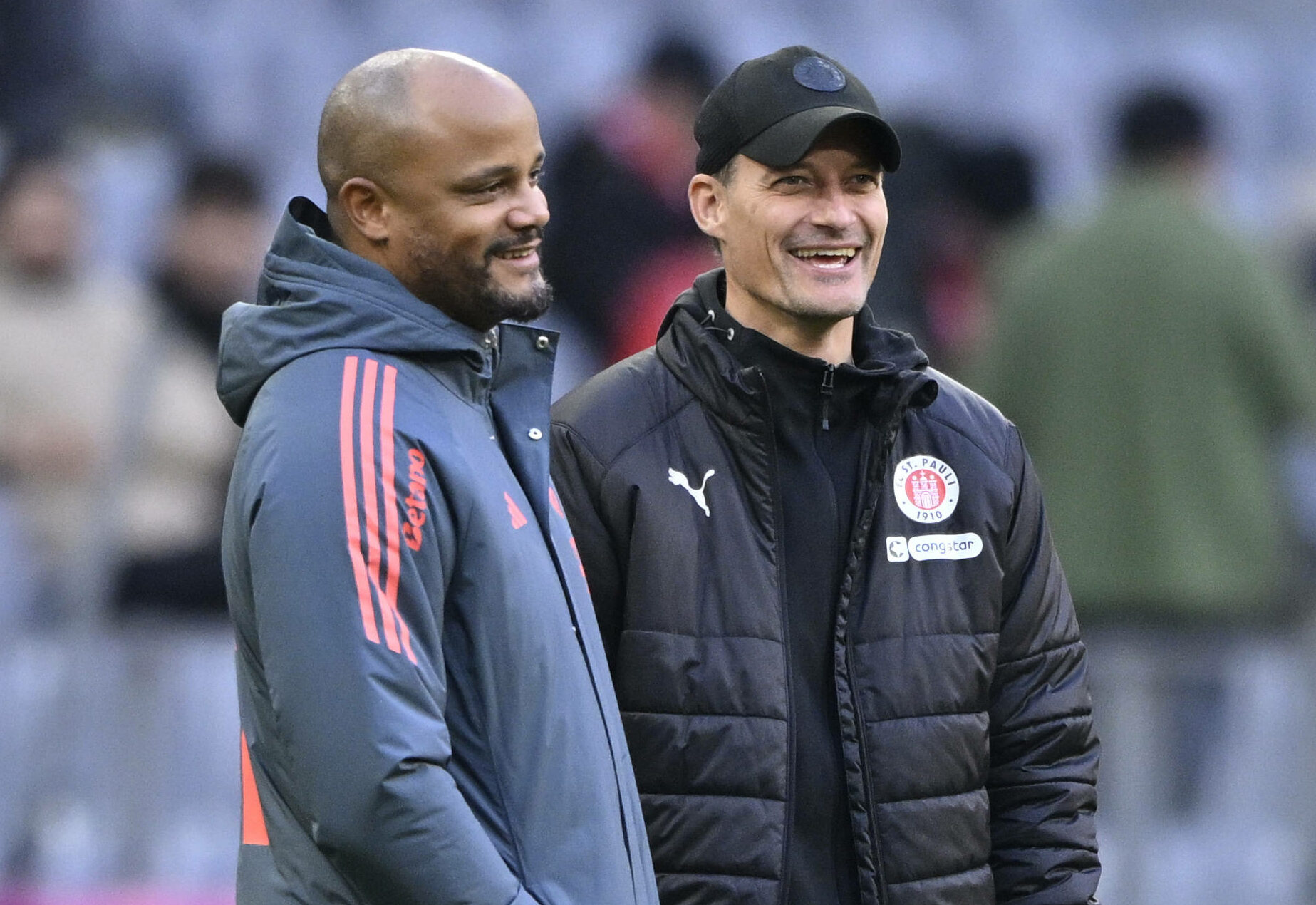 Bayern-Trainer Vincent Kompany und St. Pauli-Coach Alexander Blessin unterhalten sich und lachen dabei