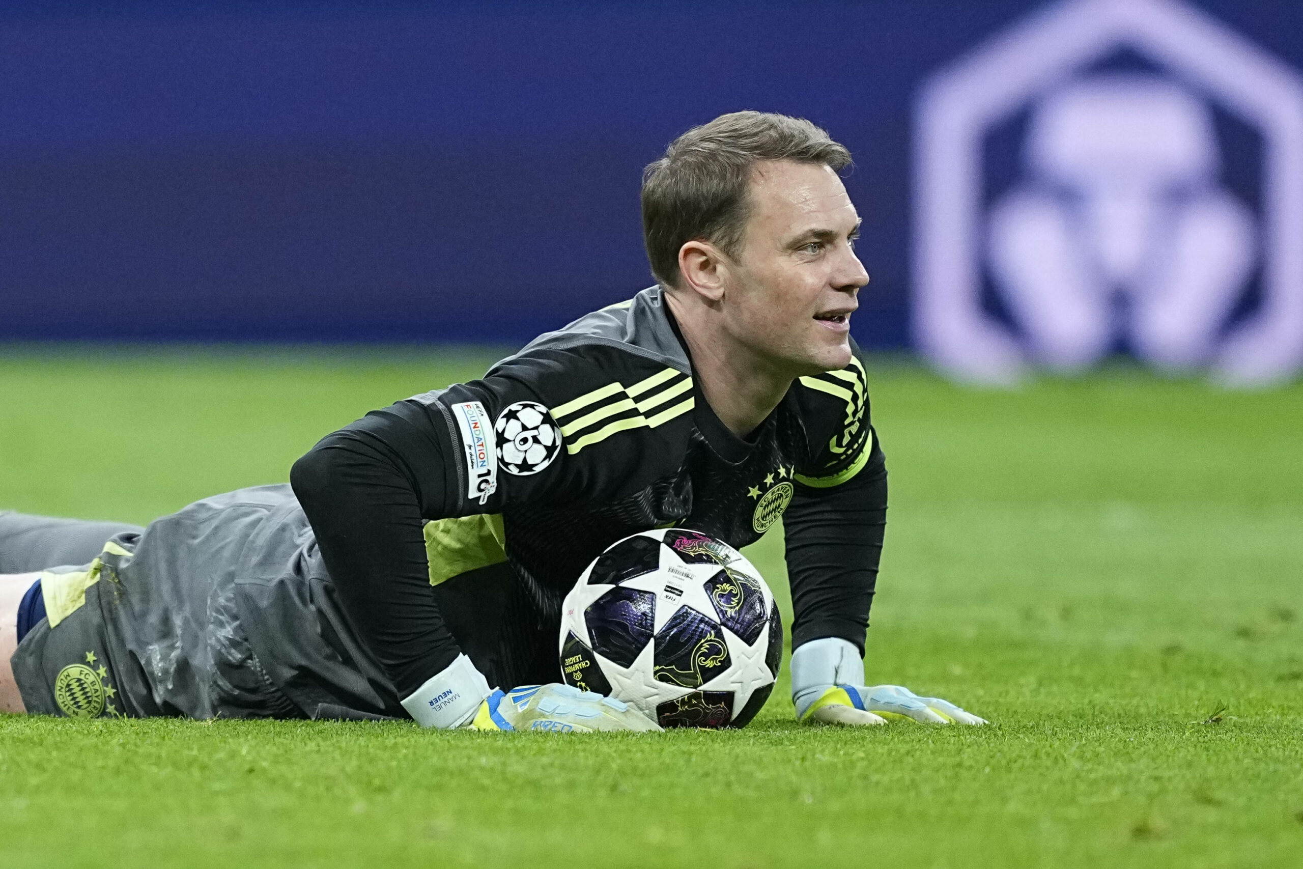 Manuel Neuer liegt nach einem gehaltenen Ball mit einem Lächeln auf dem Rasen.