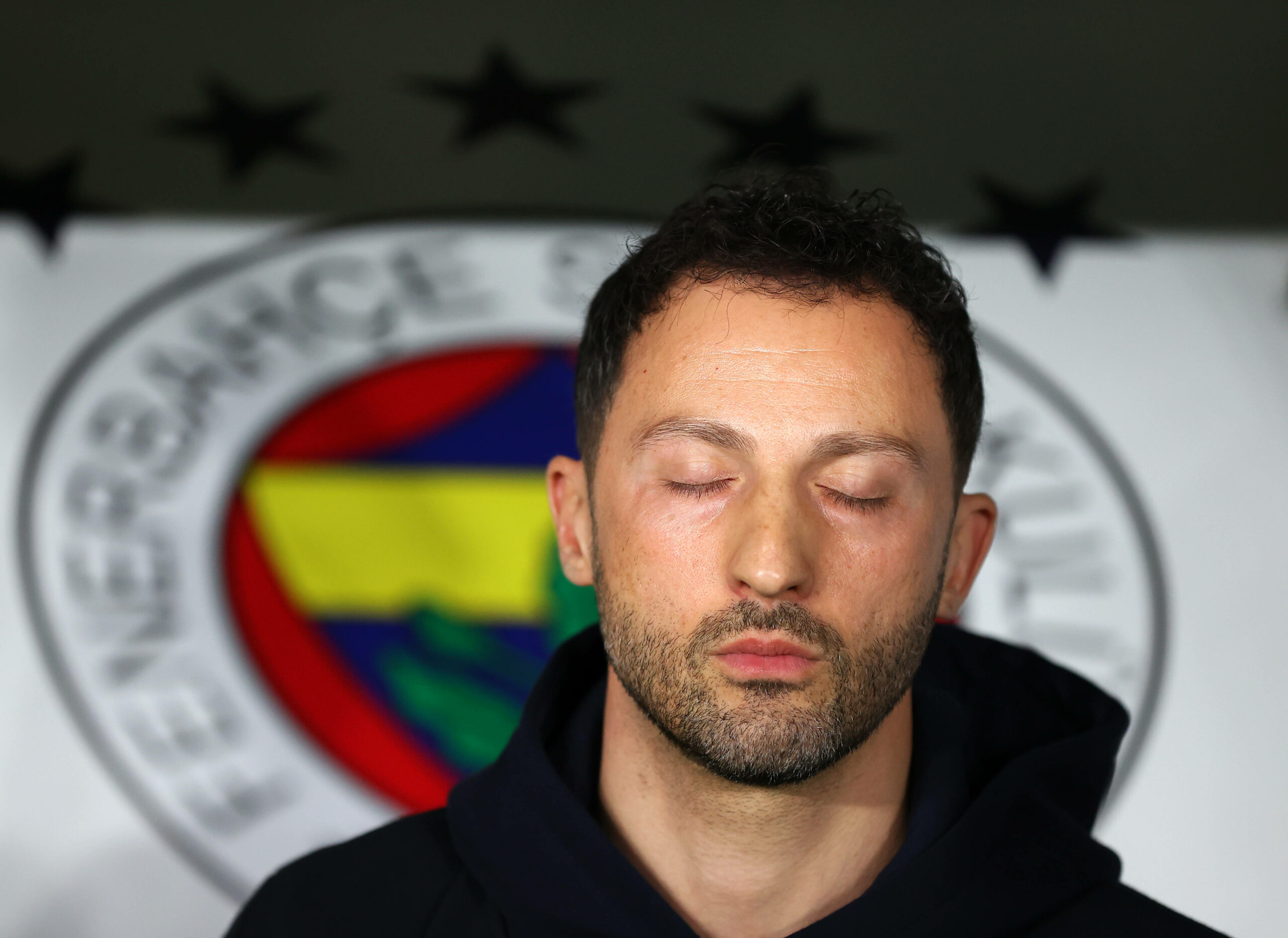 Domenico Tedesco vor dem Fenerbahce Logo mit verschlossenen Augen
