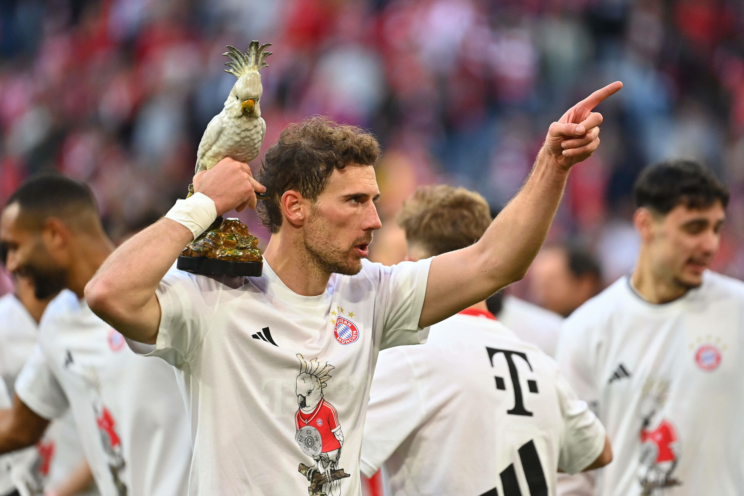 Leon Goretzka hält die Kakadu-Porzellanfigur auf der Schulter und trägt das Meistershirt 2026.