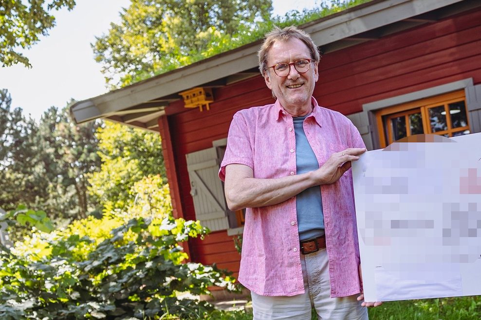 Mann in rosa Hemd vor einem Holzhaus