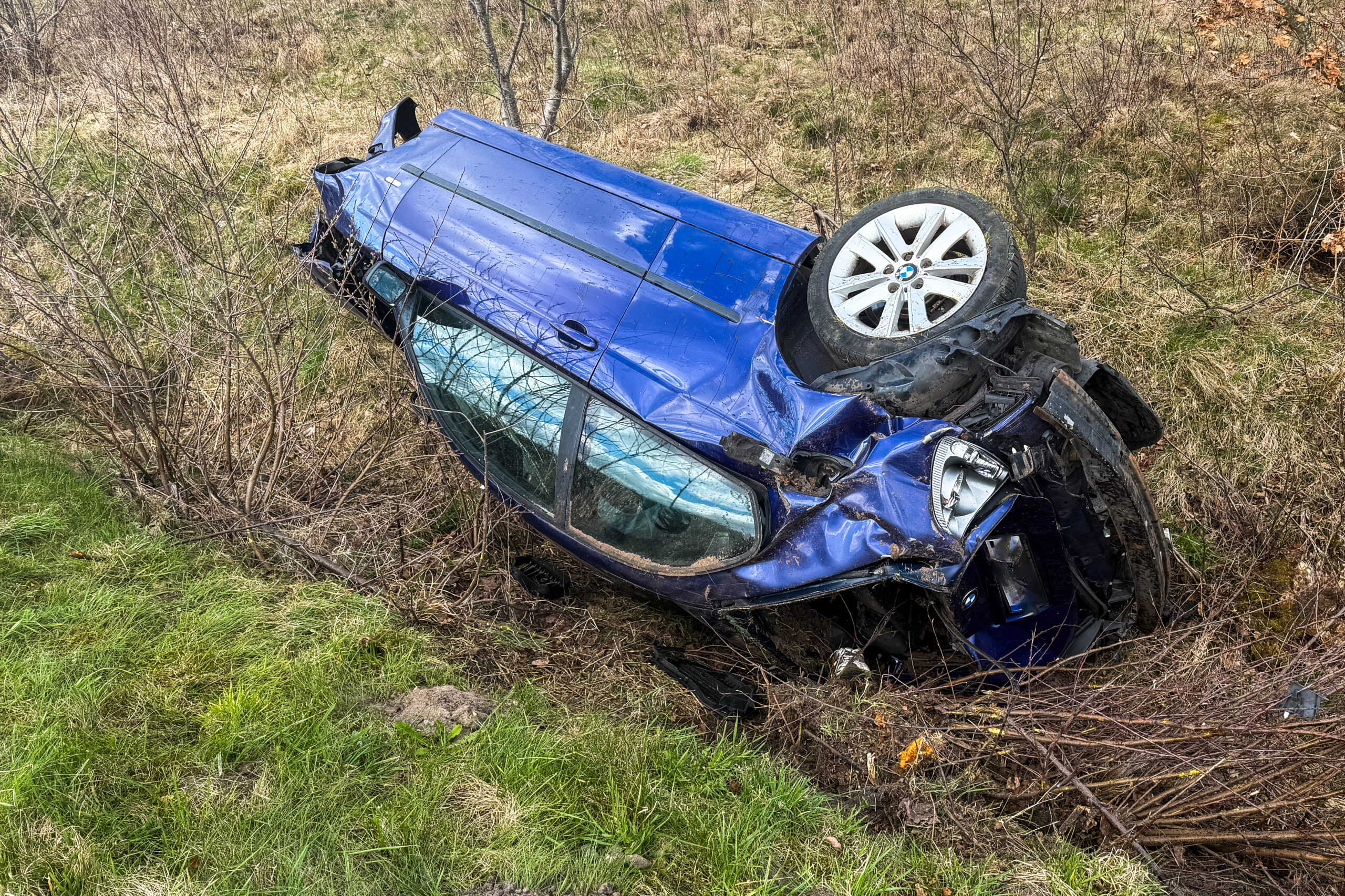Ein blaues Auto liegt stark beschädigt seitlich in einem Straßengraben.