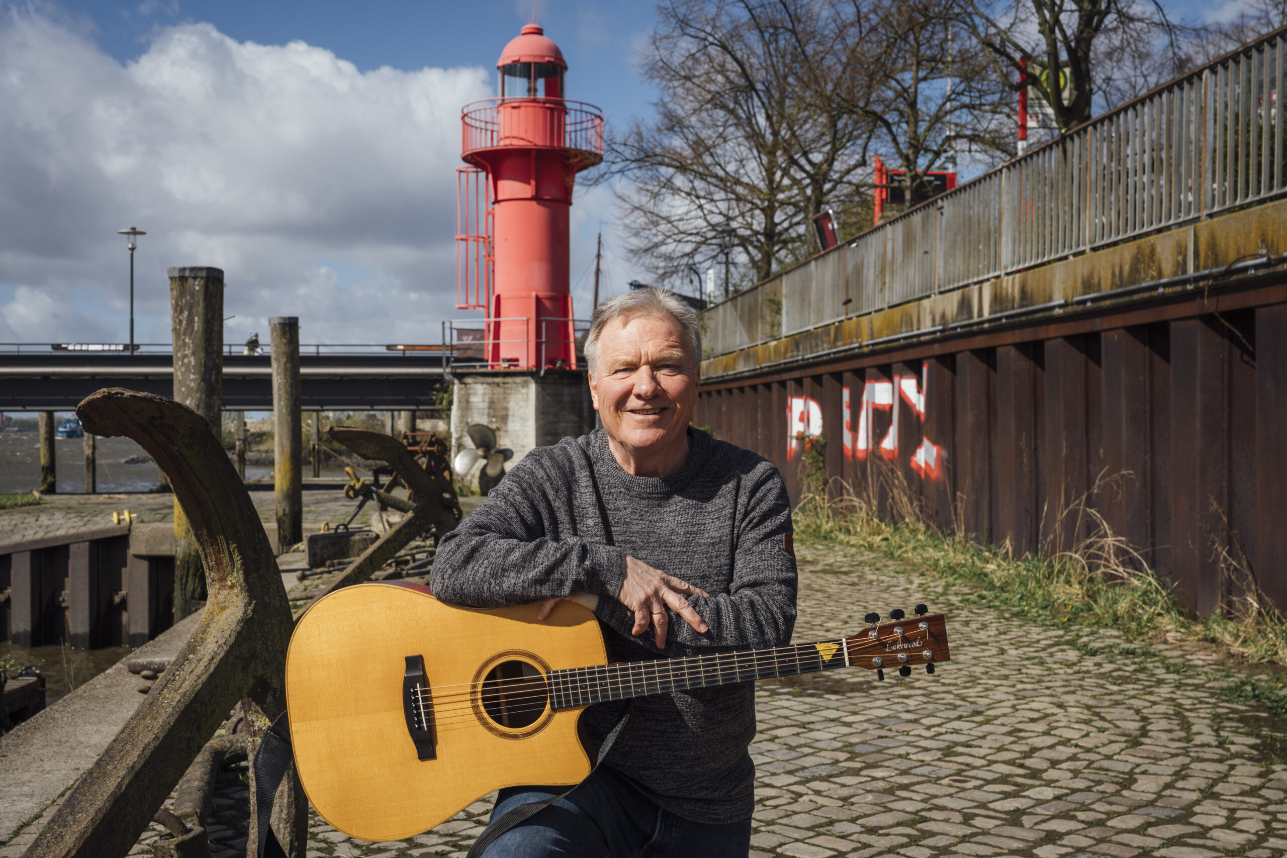 Mann mit Gitarre vor rotem Leuchtturm