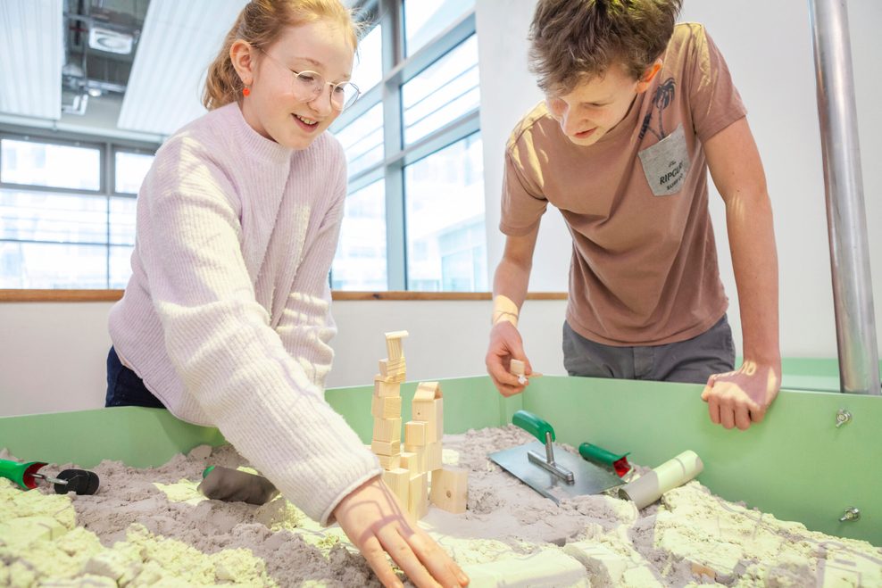 Zwei Kinder bauen mit Sand und Holzklötzen.