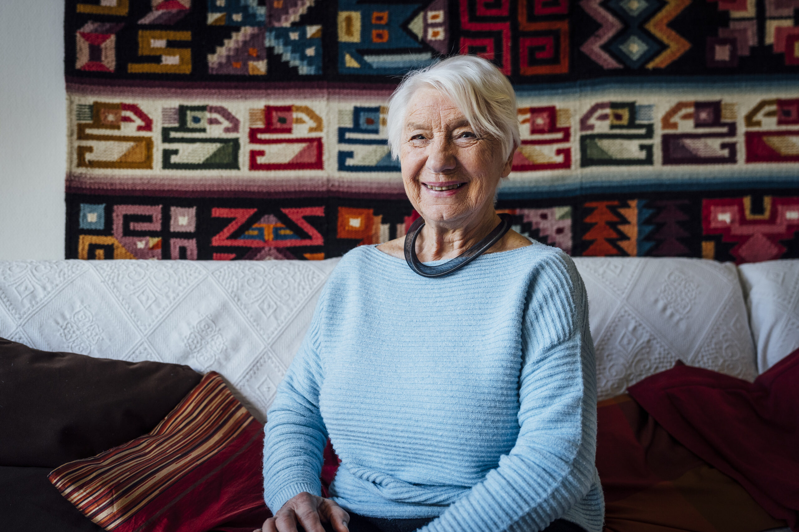 Alte Dame in blauem Pulli vor Wandteppich