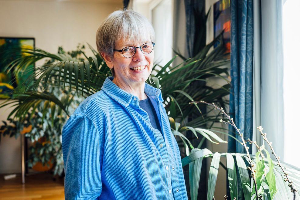 Grauhaarige Dame mit blauem Pulli vor Pflanzen