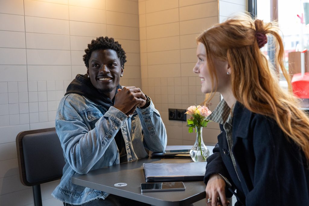 Kandidat Ibo sitzt gegenüber von Kandidatin Marlene an einem Tisch bei McDonalds.