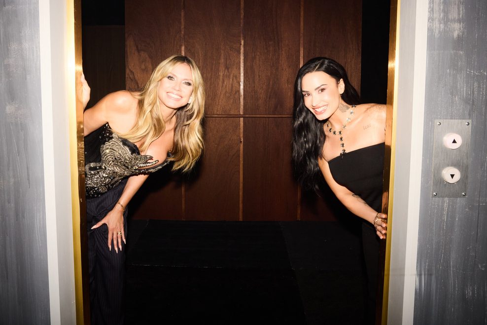 Heidi Klum und Demi Lovato schauen hinter Fahrstuhltüren hervor.