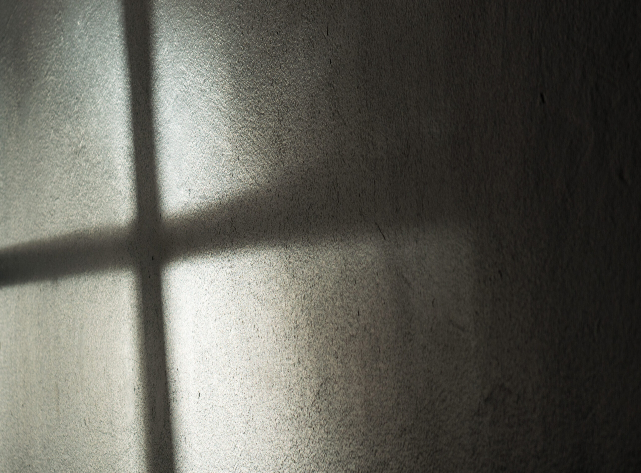 Ein Fenster wirft seinen Schatten auf die Wand. Es entsteht ein dunkles Kreuz.