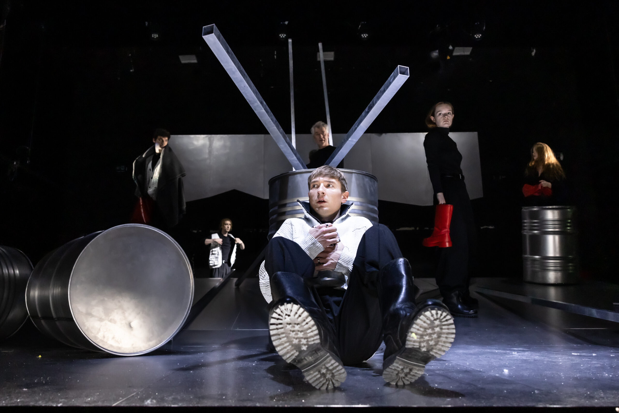 Ein Schauspieler sitzt auf der Bühne hinter einem Metallfass.