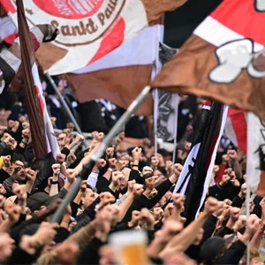 St. Pauli-Fans strecken im Block die Fäuste und schwenken mit Fahnen.