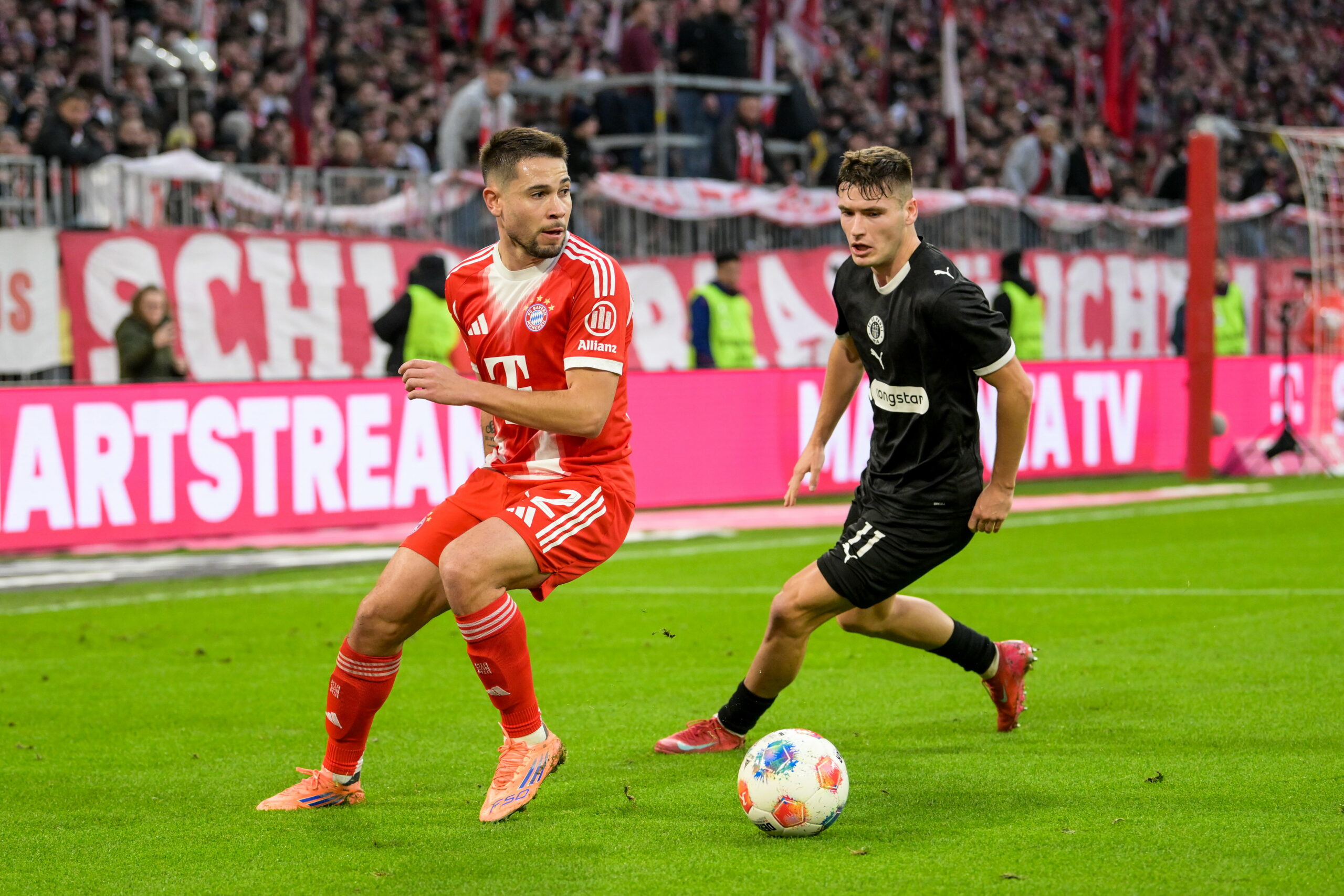 Raphael Guerreiro von Bayern München im Zweikampf mit Arkadiusz Pyrka von St. Pauli vor einer TV-Kamera von Sky