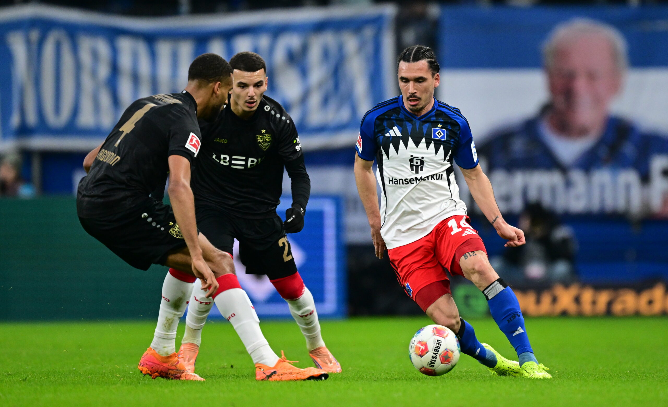 Rayan Philippe vom HSV im Zweikampf mit Josha Vagnoman und Badredine Bouanani von Stuttgart vor einer TV-Kamera von DAZN