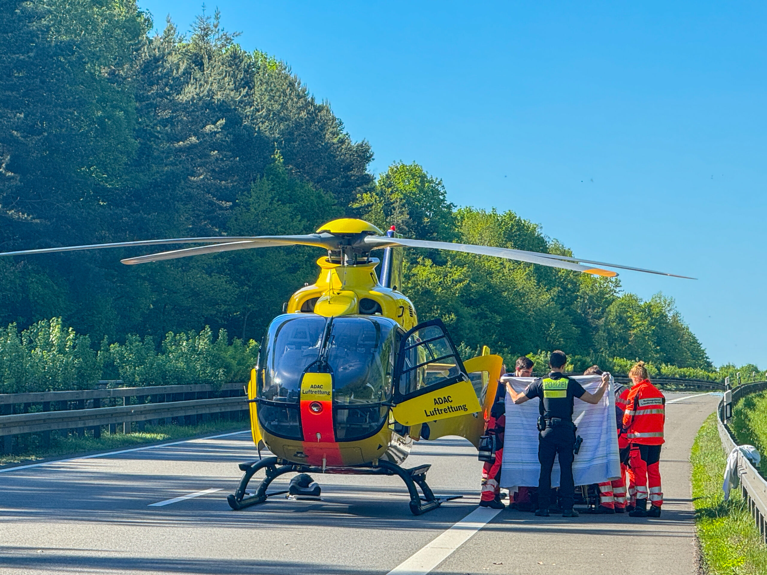 Ein Rettungshubschrauber steht auf der Autobahn. Daneben sind mehrere Einsatzkräfte.