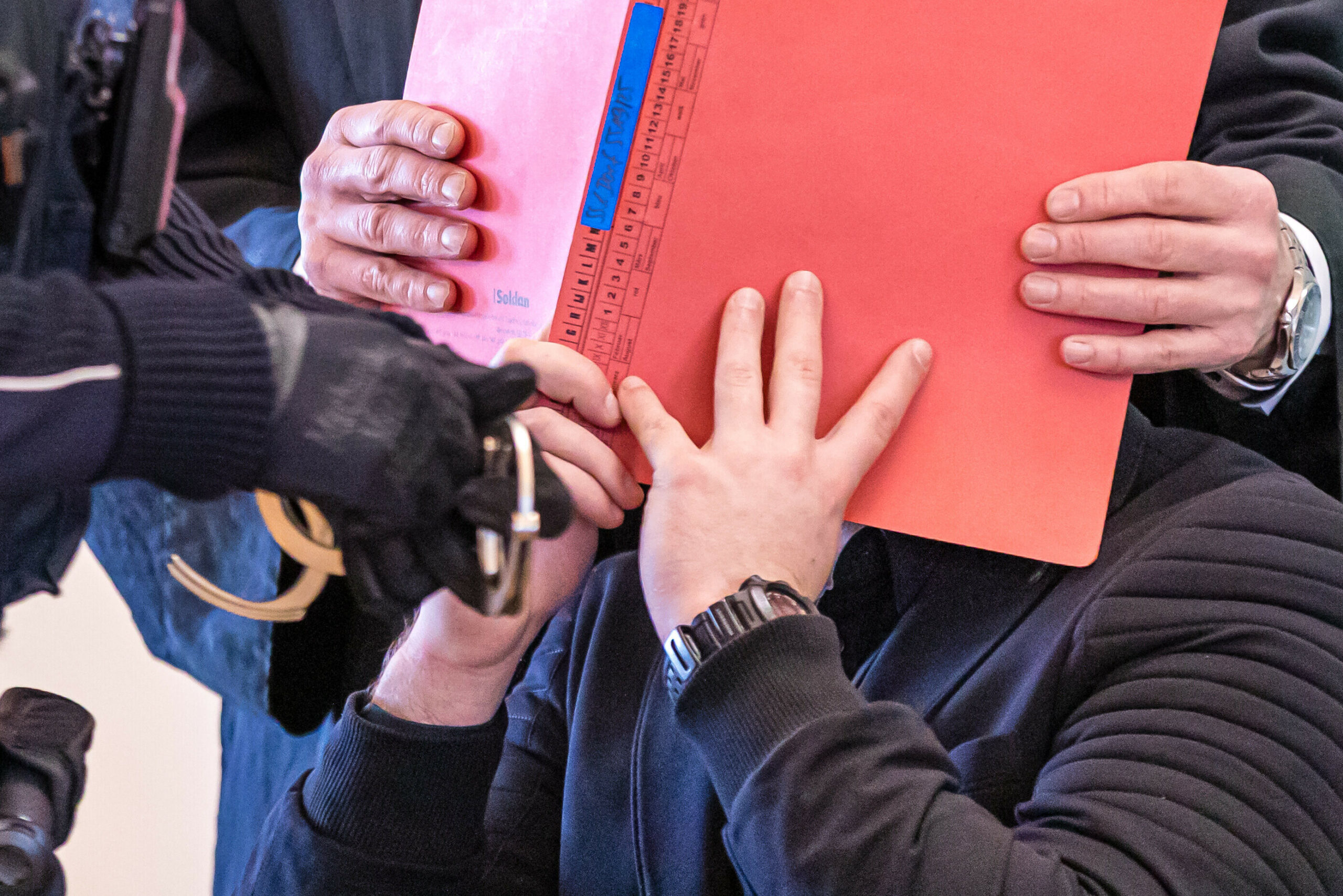 Dem Angeklagten (verdeckt) werden im Beisein seines Anwaltes (hinten) von einem Justizwachtmeister die Handschellen abgenommen.
