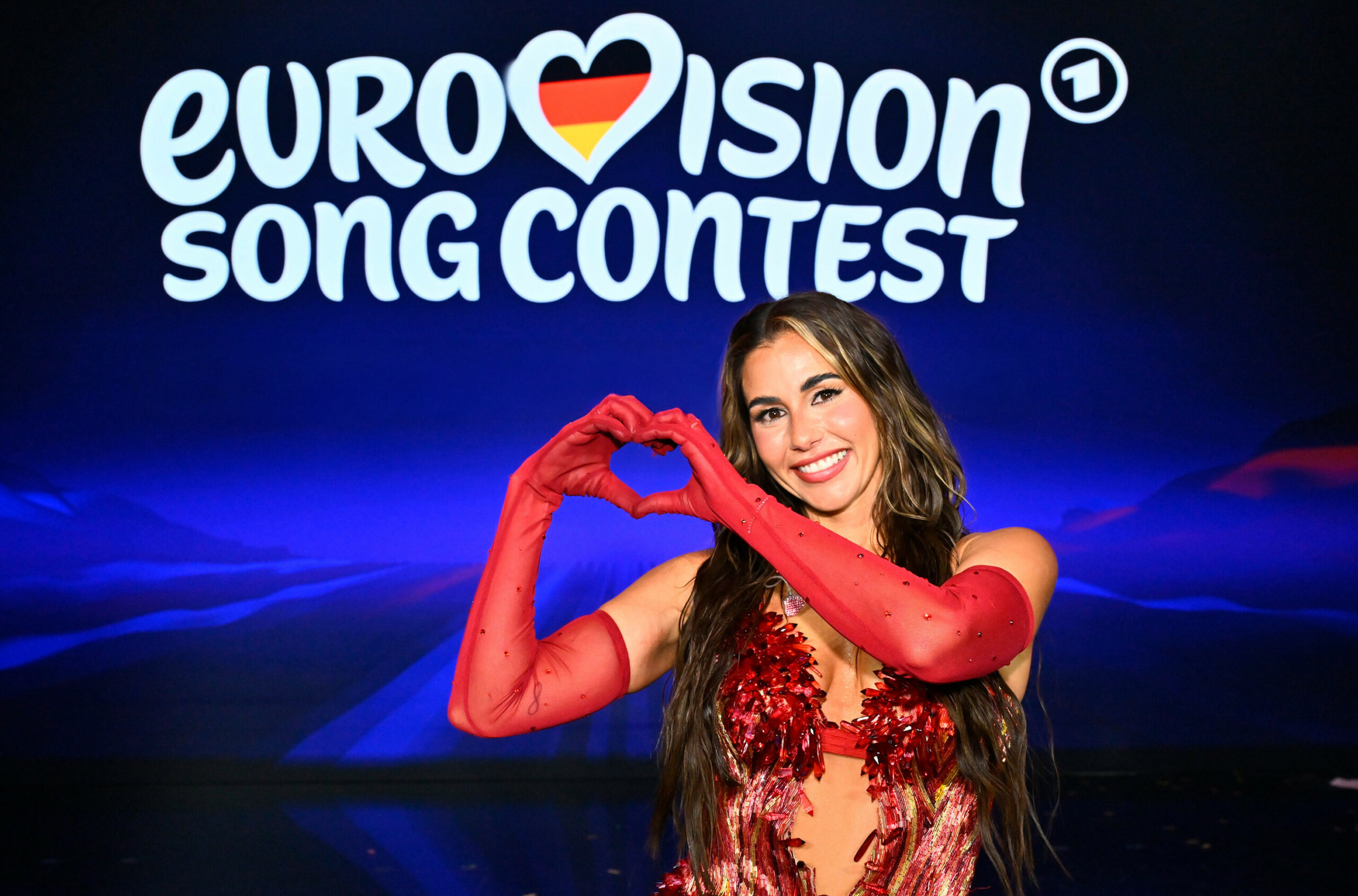 Sarah Engels vor einer blauen Wand auf der „Eurovision Song Contest“ geschrieben steht.