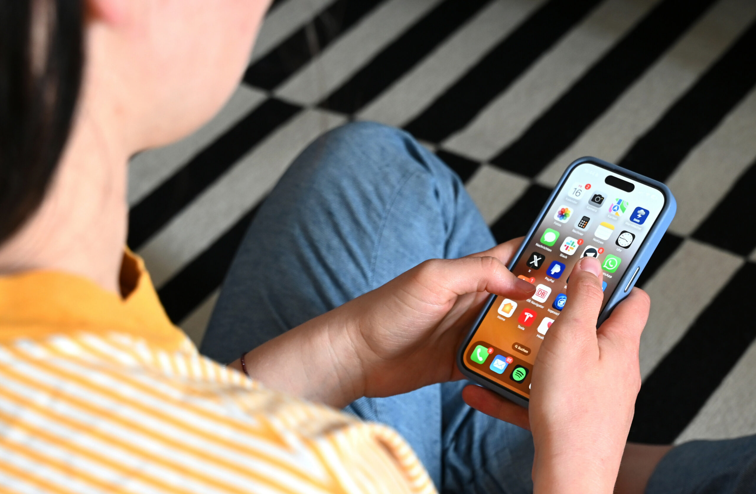 Eine Jugendliche sitzt auf dem Boden und nutzt ein Smartphone (Symbolfoto).