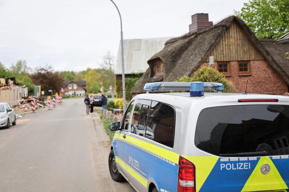 Ein Polizeiauto steht nahe einer frischen Brandruine in der Orstmitte. Eine aktuelle Brandserie verunsichert die Gemeinde Kudensee bei Brunsbüttel.