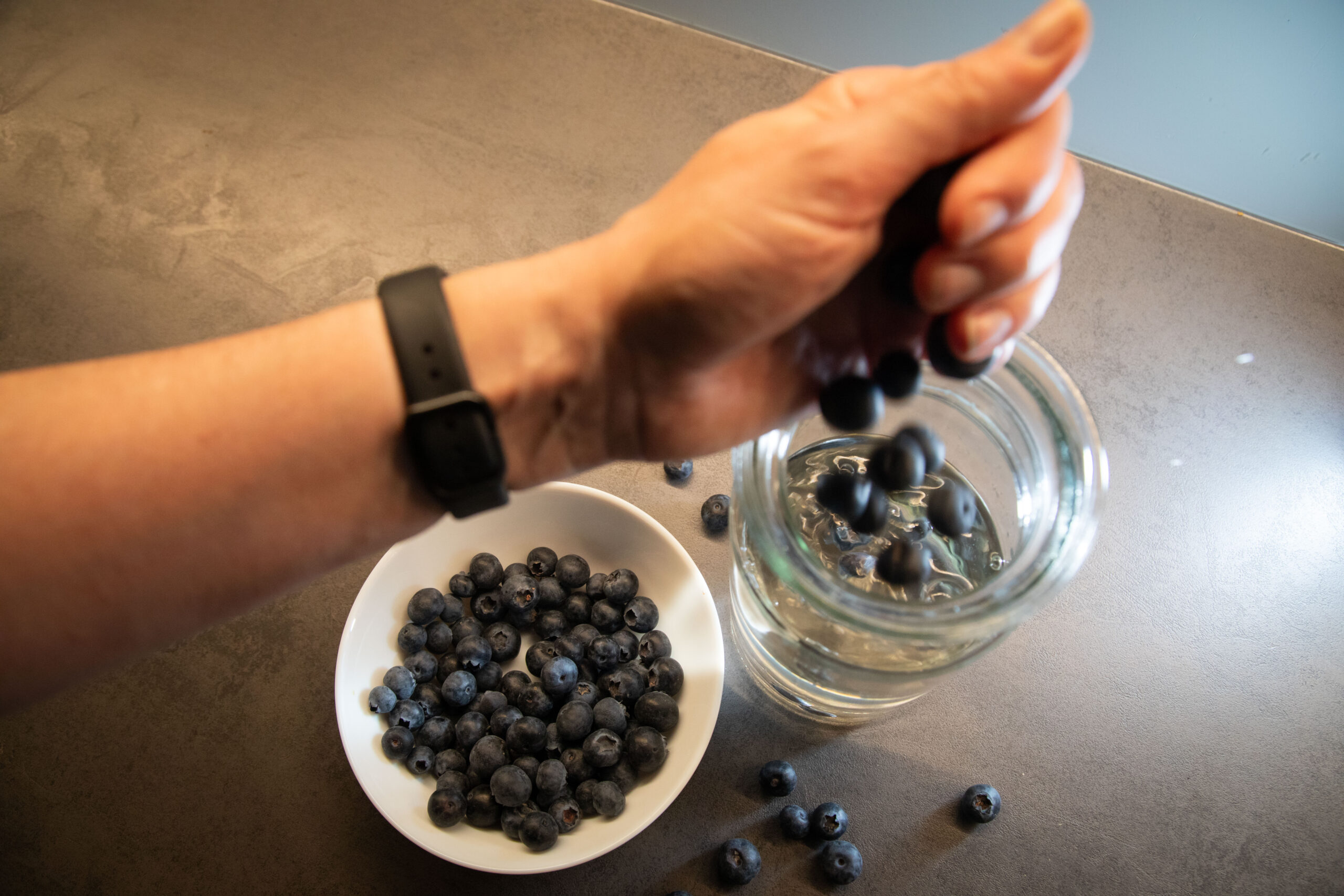 Frau gibt Blaubeeren in ein Glas mit Wasser