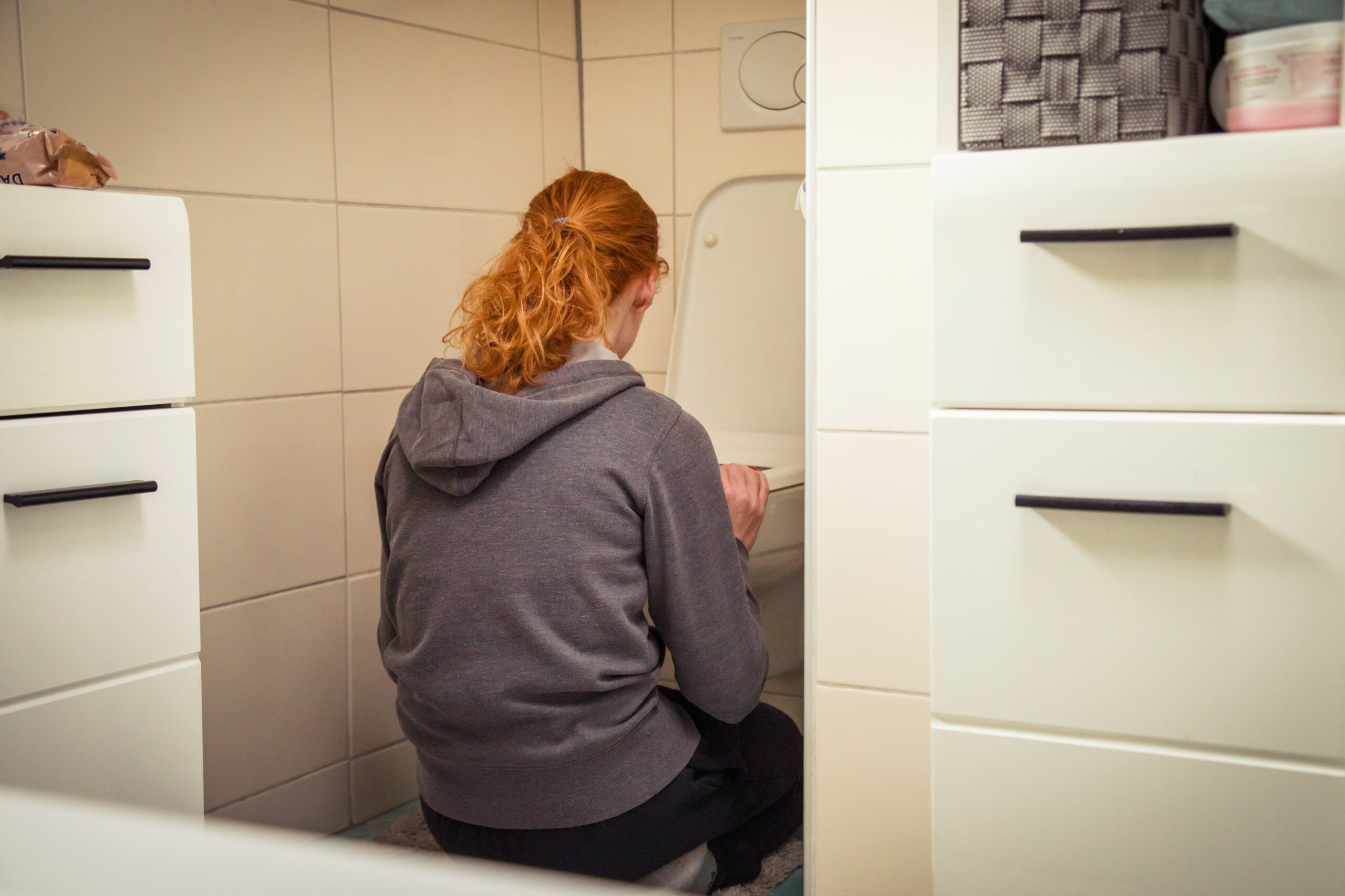 Frau hockt vor einer Toilette im Badezimmer