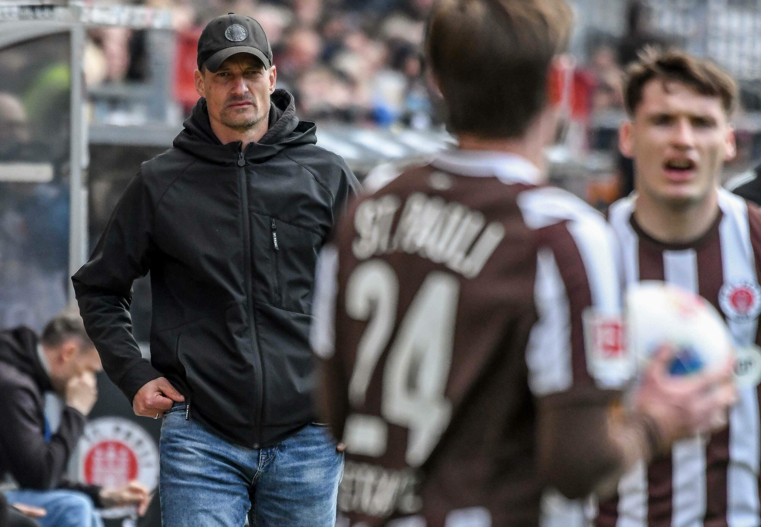 Alexander Blessin steht an der Seitenlinie und beobachtet zwei St. Pauli-Spieler beim Einwurf.