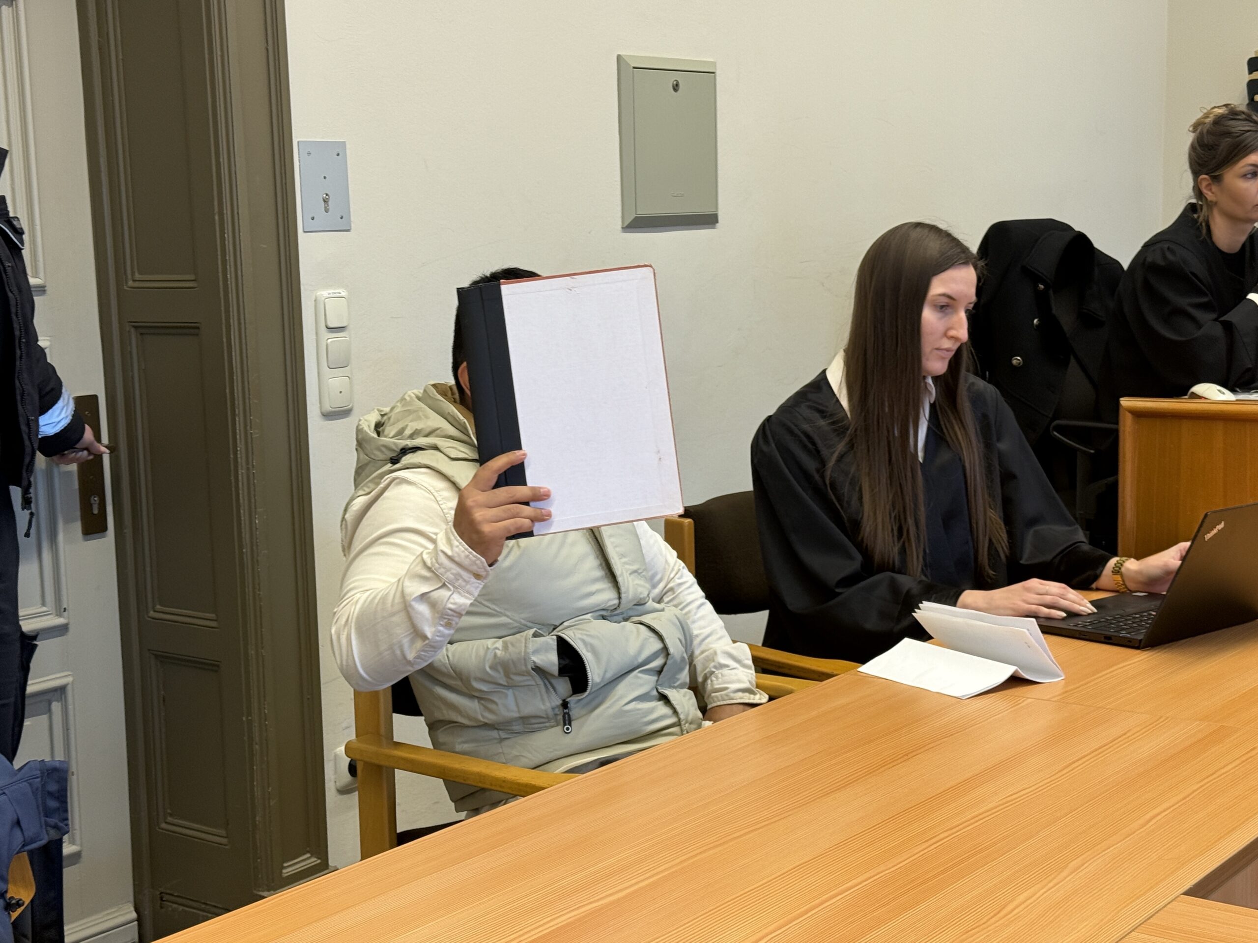 Navid M. sitzt neben seiner Verteidigerin im Landgericht. Er hält sich eine Mappe vor das Gesicht.