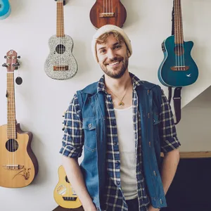 Jendrik Sigwart steht vor einer Wand mit Gitarren und Ukulelen in seiner Wohnung.