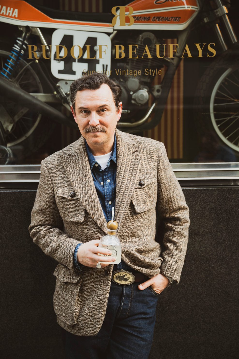 Ben Bernschneider steht vor dem Eingang des Vintage-Laden „Rudolf Beaufays“ und hält ein Getränk in der Hand.